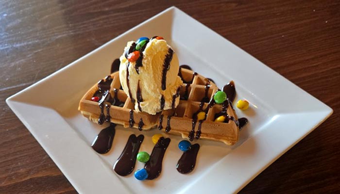 Ruby's Family Restaurant in Minnesota breakfast from the griddle featuring a waffle topped with ice cream, candy and drizzled with chocolate sauce